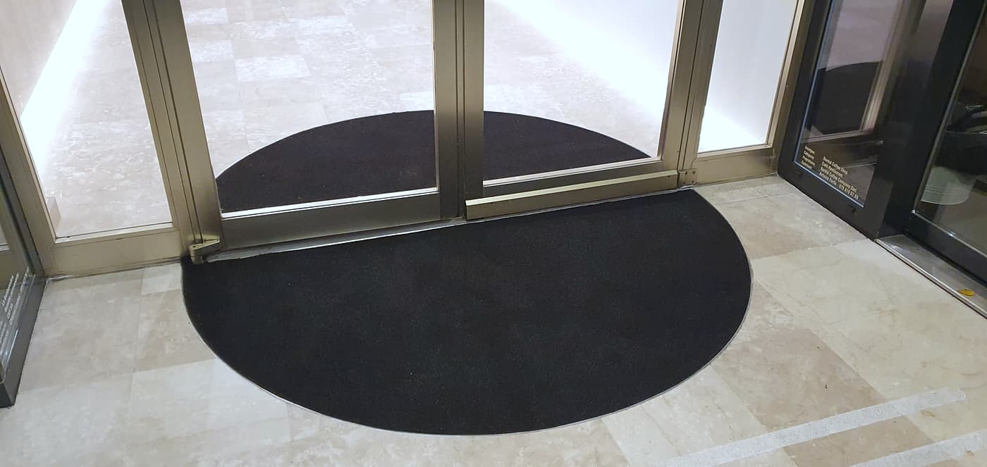 Tapis d’entrée rond encastré dans un sol en pierre, devant des portes vitrées